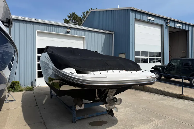 Slide: The Image of 2013 Rinker 246 Captiva Cuddy boat covered, parked outside a blue garage. - 6