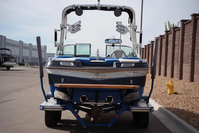 Slide: The Image of 2016 MasterCraft X10 boat on trailer, rear view, parked near industrial buildings. - 3