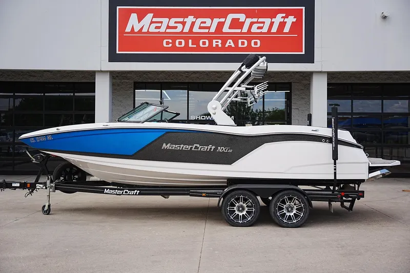 The Image of 2019 MasterCraft NXT22 boat on trailer at dealership, featuring sleek blue and white design. - 1