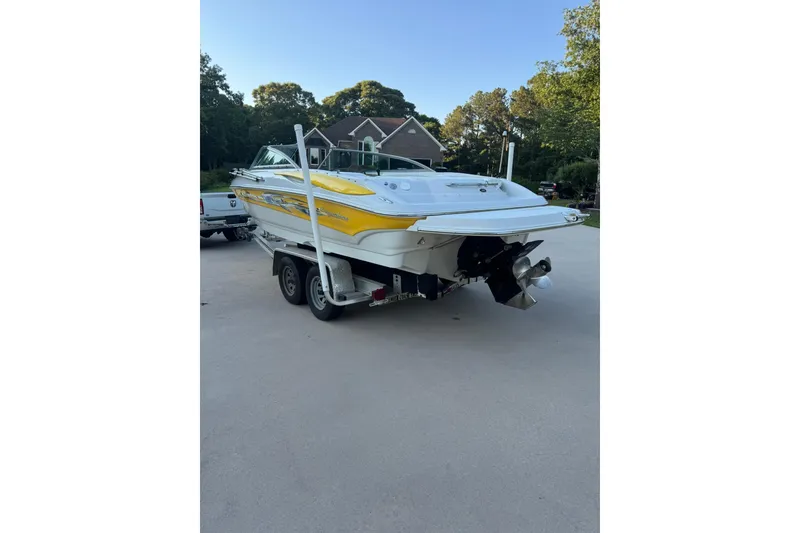 Slide: The Image of 2005 Crownline 210 Razor boat on trailer, parked in driveway, with yellow and white design. - 3