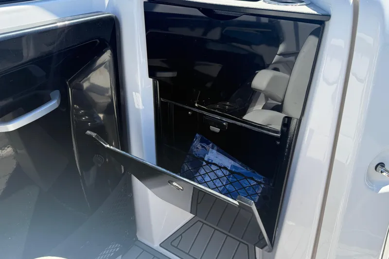 Slide: The Image of 2023 Yamaha Boats AR250 interior storage compartment with open door, showcasing seating and storage space. - 26