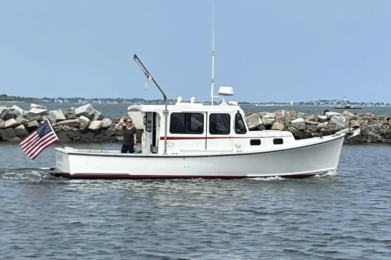 The Image of 1988 Duffy 31 Lobster Boat cruising near rocky shoreline with American flag. - 0