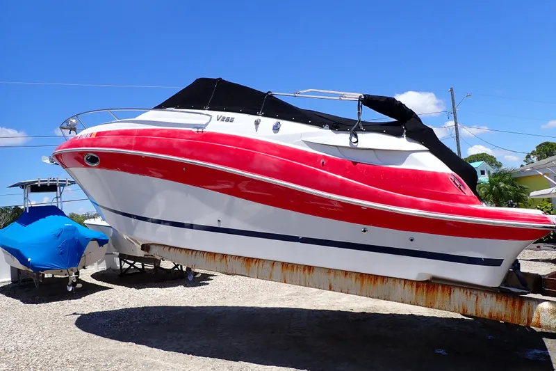 The Image of 2012 Four Winns V265 boat with red and white hull on a trailer under blue sky. - 0