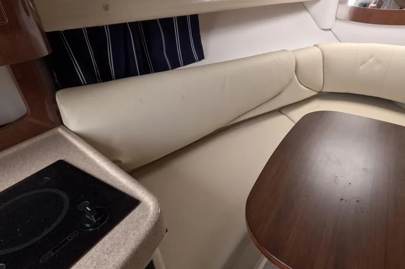 Slide: The Image of 2012 Four Winns V265 interior with beige seating, wooden table, and compact kitchen area. - 57