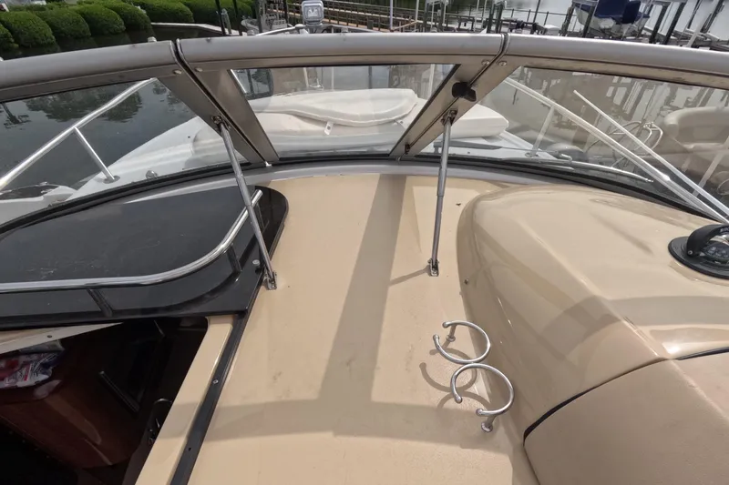 Slide: The Image of 2012 Four Winns V265 boat deck with windshield and cup holders, docked by water. - 66