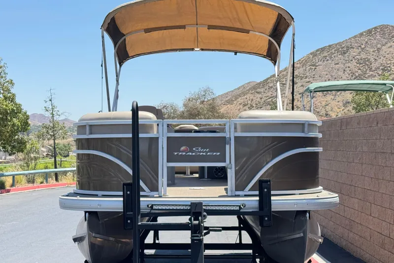 Slide: The Image of 2024 Sun Tracker SportFish 22 DLX pontoon boat with canopy, parked outdoors. - 2