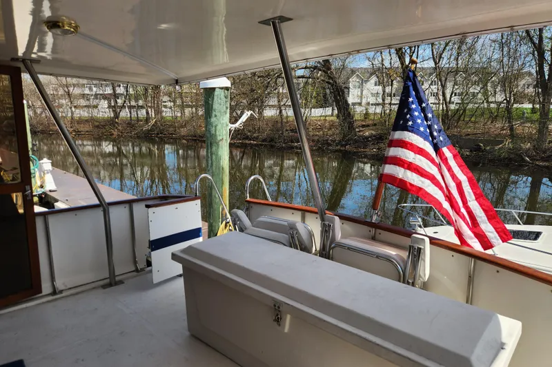 Slide: The Image of 1987 Jefferson 42 SE Sundeck Motor Yacht with American flag, docked by a serene river. - 12
