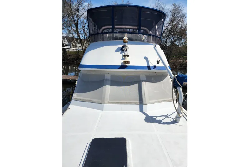 Slide: The Image of 1987 Jefferson 42 SE Sundeck Motor Yacht with blue accents, docked near trees. - 4
