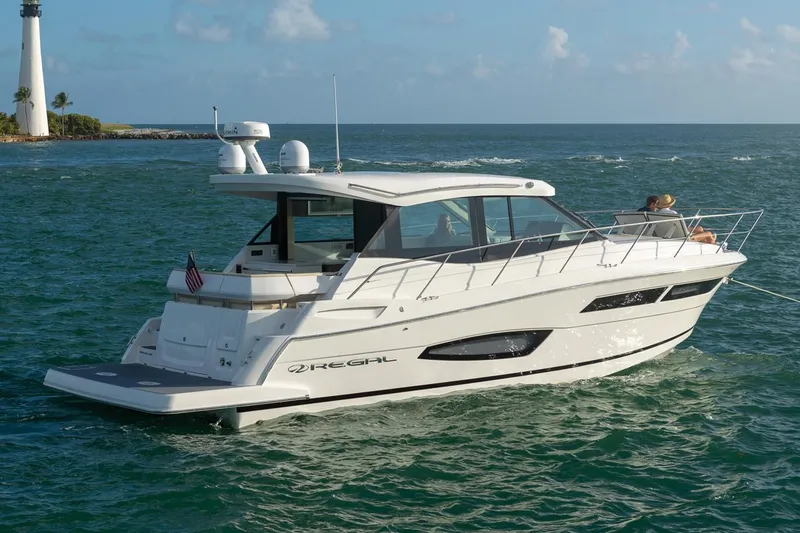 Slide: The Image of Manufacturer Provided Image: 2026 Regal 38 Grande Coupe yacht cruising near a lighthouse on a sunny day. - 2