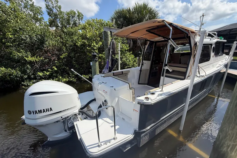 The Image of 2019 Ranger Tugs R-27 boat docked, featuring a Yamaha outboard motor, surrounded by lush greenery. - 0