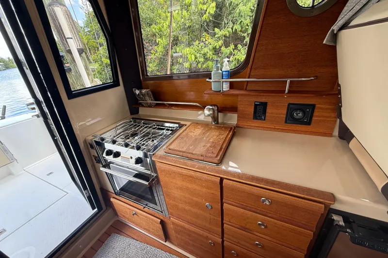 Slide: The Image of 2019 Ranger Tugs R-27 boat kitchen with stove, sink, and wooden cabinetry. - 20
