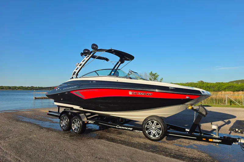 Slide: The Image of 2024 Crownline Eclipse E255 SURF boat on trailer by a lake under clear blue sky. - 7