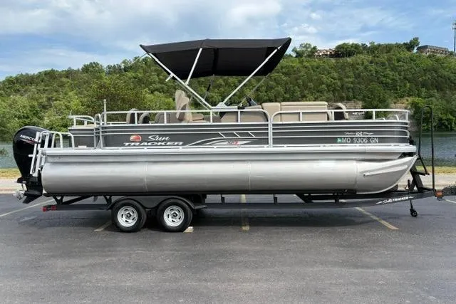 The Image of 2022 Sun Tracker Fishin' Barge 22 XP3 pontoon boat on trailer, parked outdoors. - 0