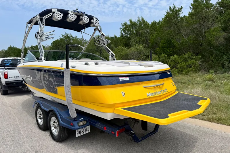 Slide: The Image of 2009 MasterCraft X30 boat on trailer, vibrant yellow and blue design, parked roadside. - 11