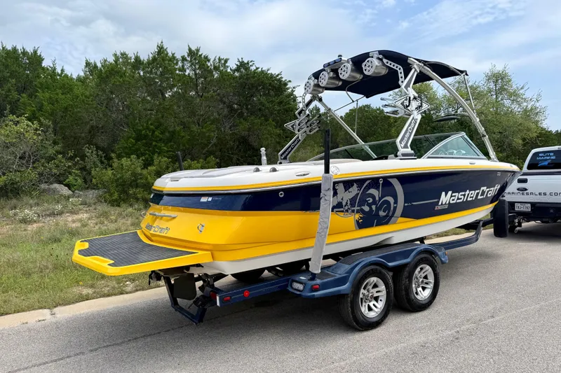 Slide: The Image of 2009 MasterCraft X30 boat on trailer, vibrant yellow and blue design, parked roadside. - 14