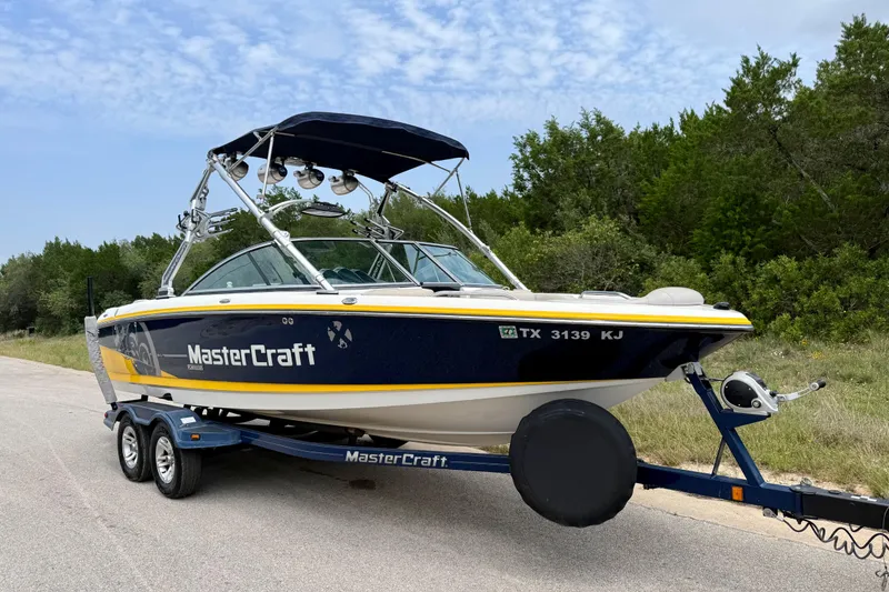 Slide: The Image of 2009 MasterCraft X30 boat on trailer, parked on roadside with trees in background. - 16
