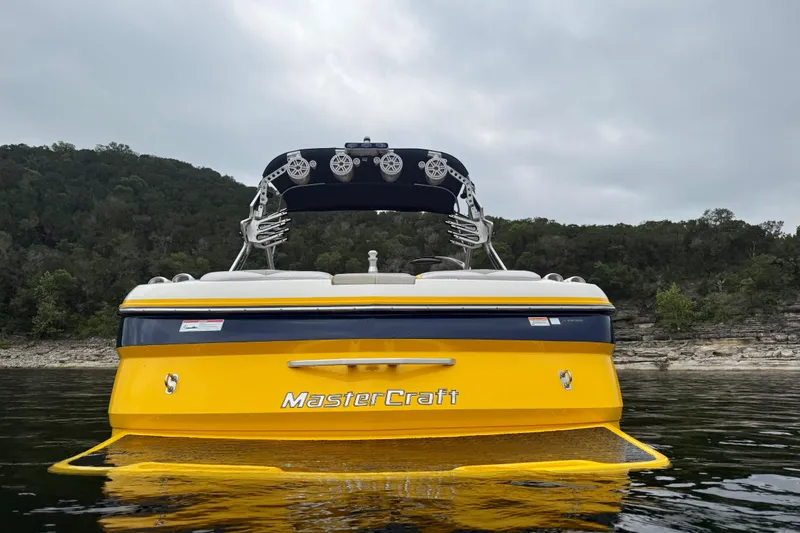 Slide: The Image of 2009 MasterCraft X30 boat on water, yellow hull, overcast sky, forested shoreline. - 5