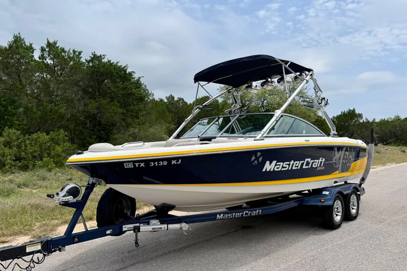 Slide: The Image of 2009 MasterCraft X30 boat on trailer, parked on roadside with trees in background. - 9