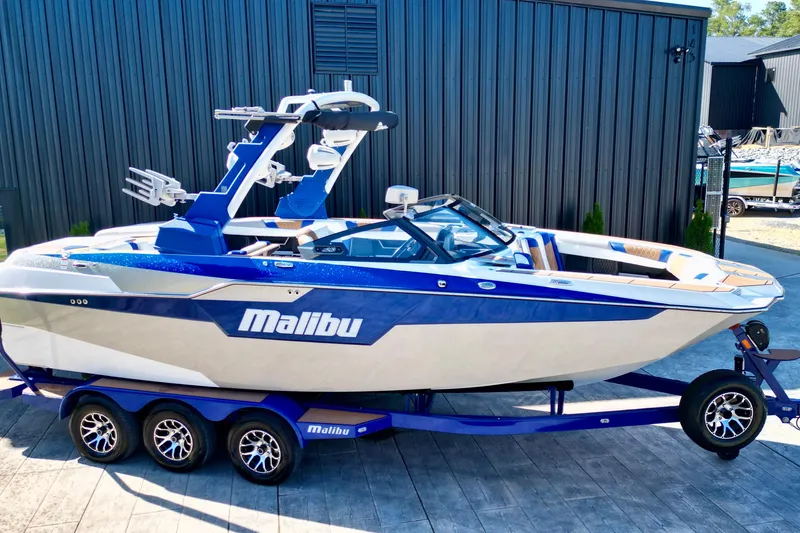 The Image of 2022 Malibu M240 boat on trailer, blue and white design, parked outdoors. - 1
