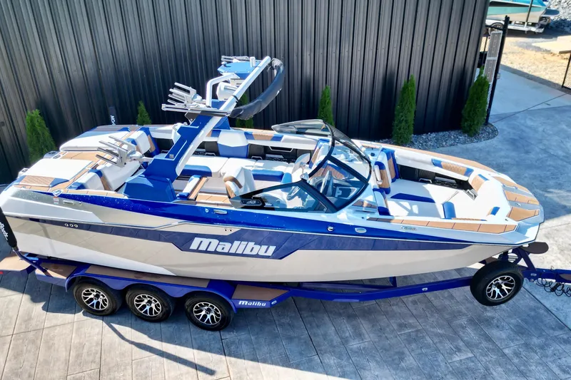 Slide: The Image of 2022 Malibu M240 boat on trailer, blue and white design, parked outdoors. - 2