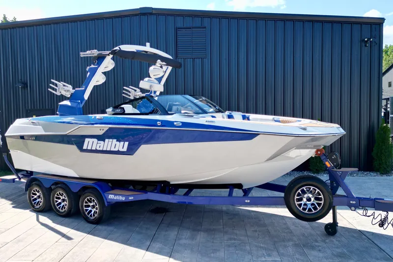 Slide: The Image of 2022 Malibu M240 boat on trailer, blue and white design, parked outdoors. - 3