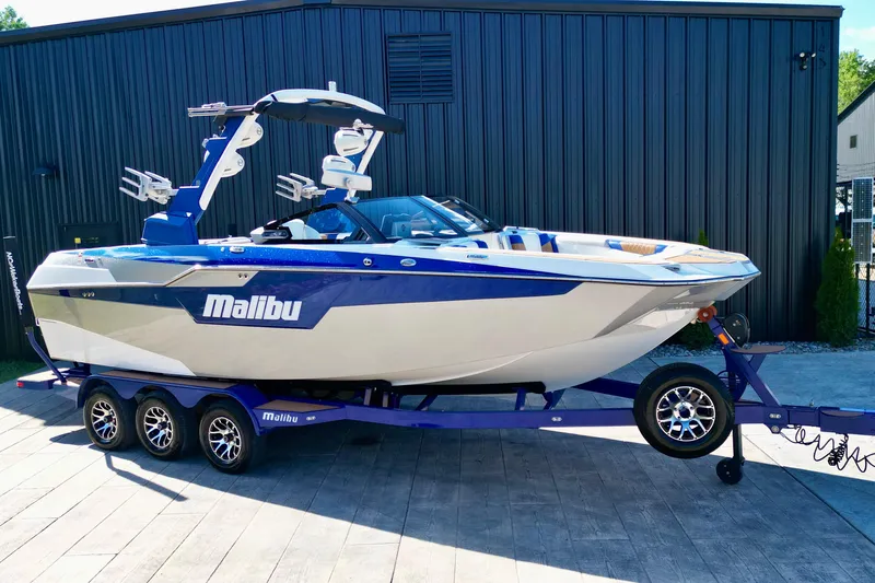 Slide: The Image of 2022 Malibu M240 boat on trailer, blue and white design, parked outdoors. - 5