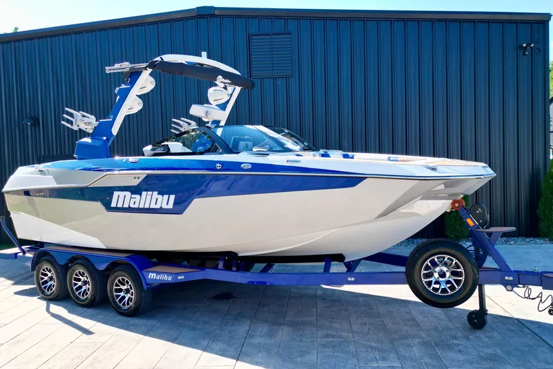 Slide: The Image of 2022 Malibu M240 boat on trailer, blue and white design, parked outdoors. - 6