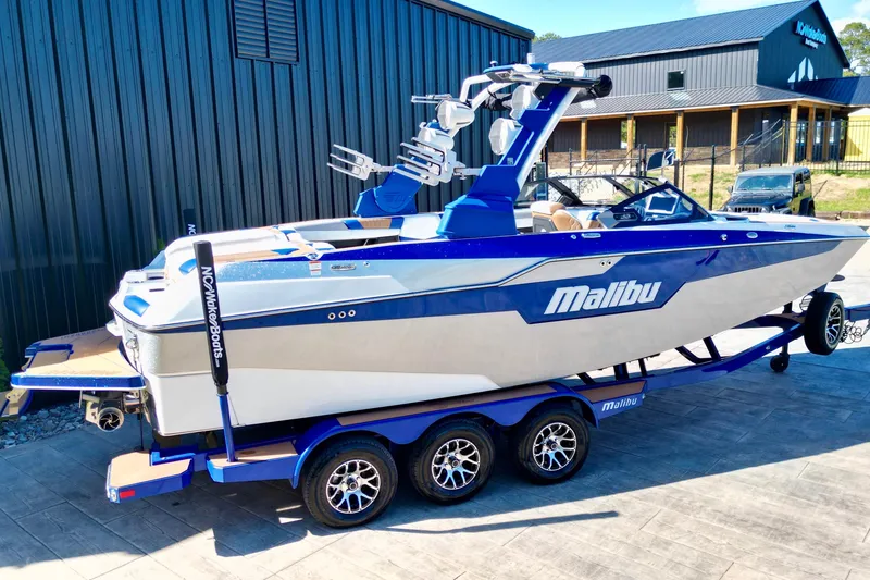 Slide: The Image of 2022 Malibu M240 boat on trailer, blue and white design, parked outdoors. - 8