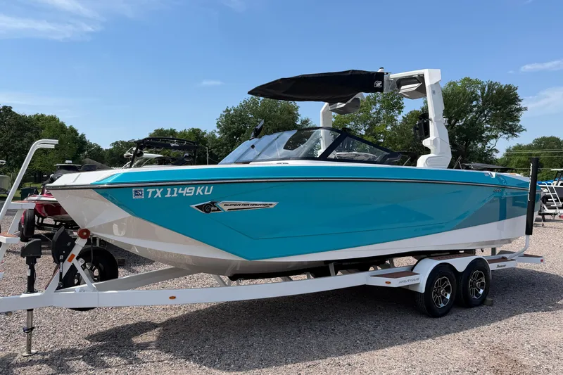 Slide: The Image of 2023 Nautique Super Air Nautique G25 boat on trailer, vibrant blue color, parked outdoors. - 2