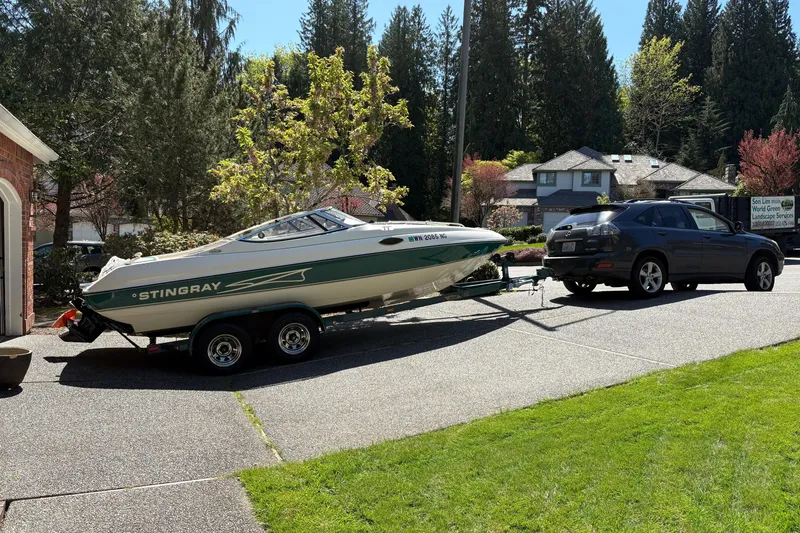 Slide: The Image of 1997 Stingray 200 CS boat on trailer, hitched to a dark SUV in a suburban driveway. - 5