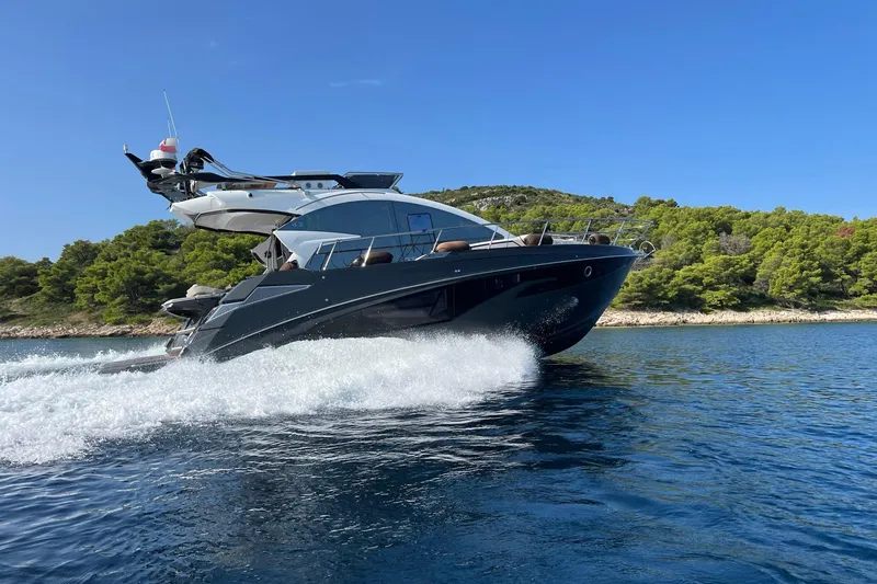 Slide: The Image of 2026 Cobrey 45 FLY yacht cruising on blue water near a forested shoreline. - 2