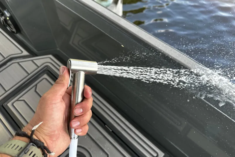 Slide: The Image of Hand holding a spray nozzle on a 2024 H-Craft 27 CC boat deck. - 25