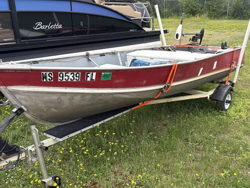The Image of A red and silver boat on a trailer, surrounded by grass and flowers. - 1