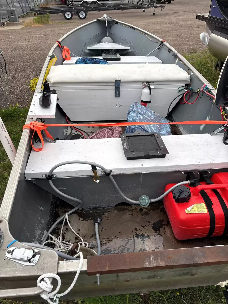 Slide: The Image of An open aluminum boat with benches, coolers, and a gas tank, parked on a lot. - 4