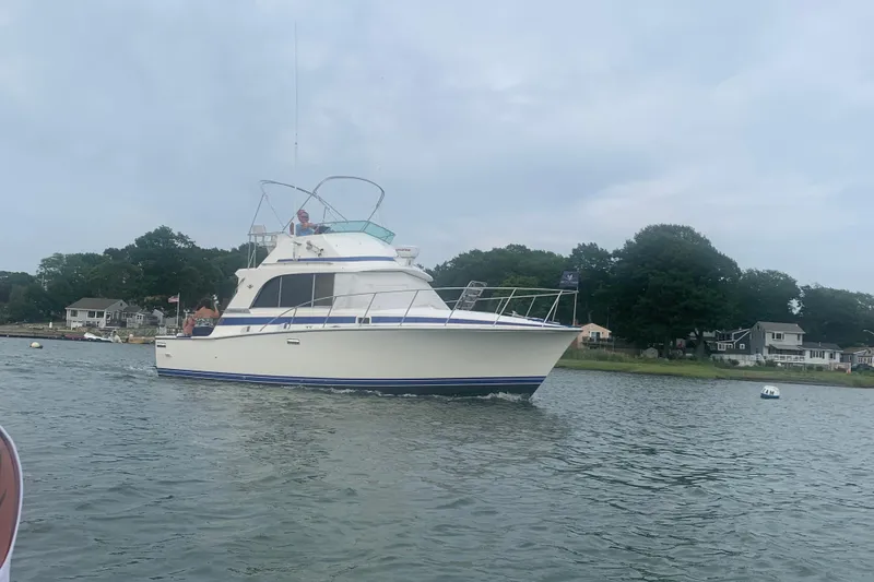 Slide: The Image of 1985 Bertram 33 Flybridge Cruiser on calm water near shoreline homes. - 1