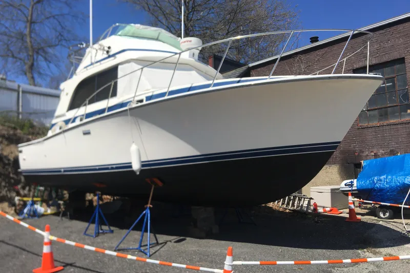 Slide: The Image of 1985 Bertram 33 Flybridge Cruiser on stands, outdoors, with safety cones and blue sky. - 2