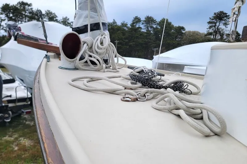 Slide: The Image of 1974 Marshall 22 Catboat deck with ropes and fittings, surrounded by trees and other boats. - 24