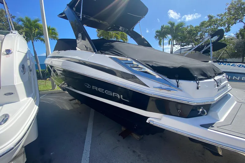 Slide: The Image of 2013 Regal 27 FasDeck RX boat with black cover, parked outdoors under sunny skies. - 2