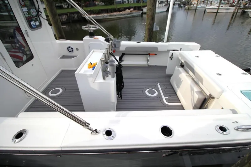 Slide: The Image of 2023 Parker 2320 Sport Cabin boat deck with fishing rod holders and seating, docked by the water. - 11
