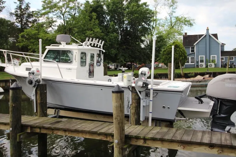 Slide: The Image of 2023 Parker 2320 Sport Cabin boat docked near a blue house, surrounded by trees. - 3