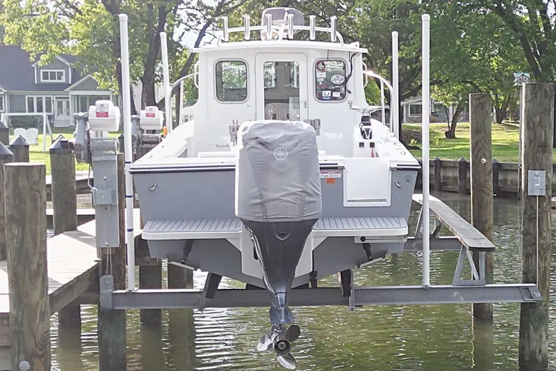 Slide: The Image of 2023 Parker 2320 Sport Cabin boat docked on a lift, surrounded by trees and houses. - 4