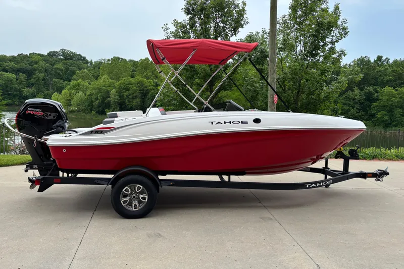 The Image of 2026 Tahoe T18 boat with red hull and canopy on a trailer, parked outdoors. - 0