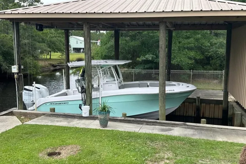 Slide: The Image of 2022 Aquasport 2500 Center Console boat docked under a covered structure by a river. - 3