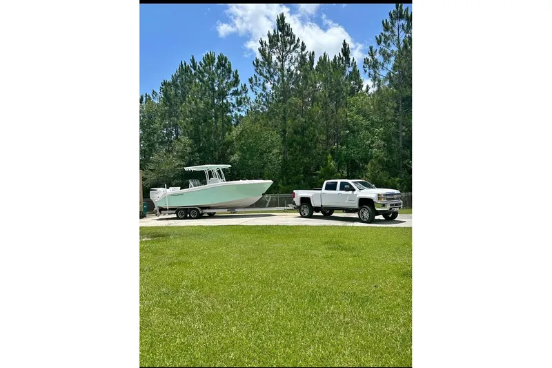 Slide: The Image of 2022 Aquasport 2500 Center Console boat on trailer, towed by a white truck, surrounded by trees. - 4