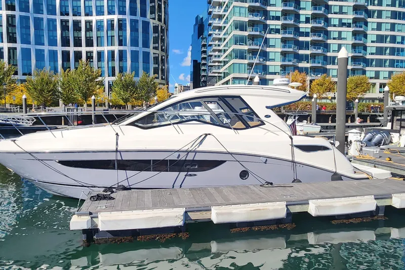 Slide: The Image of 2019 Sea Ray Sundancer 350 Coupe docked at a marina with modern buildings in the background. - 2