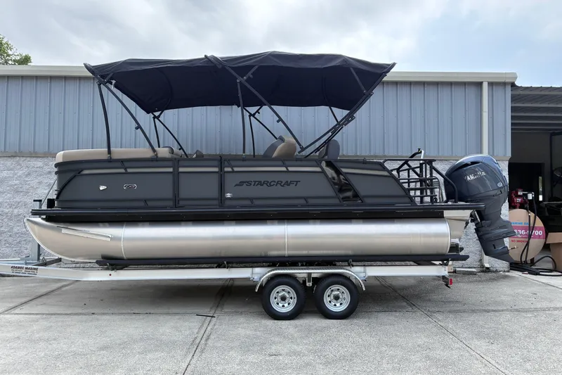The Image of 2026 Starcraft EXS 1 Q DH pontoon boat on trailer, parked outside a building. - 0