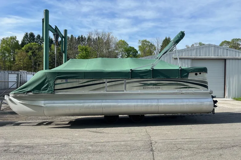 Slide: The Image of 2004 Bennington 2250RL pontoon boat with green cover, parked outdoors near a metal building. - 9