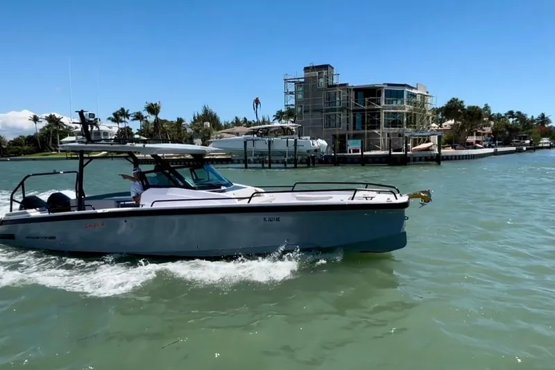 The Image of 2025 Axopar 29 Sun-Top boat cruising near waterfront homes under clear blue sky. - 1