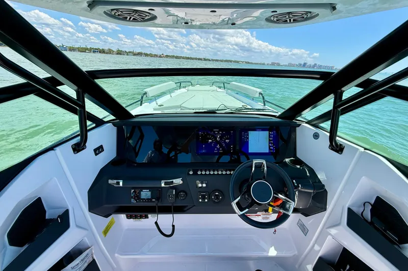 Slide: The Image of 2025 Axopar 29 Sun-Top boat dashboard with steering wheel and navigation screens on open water. - 12