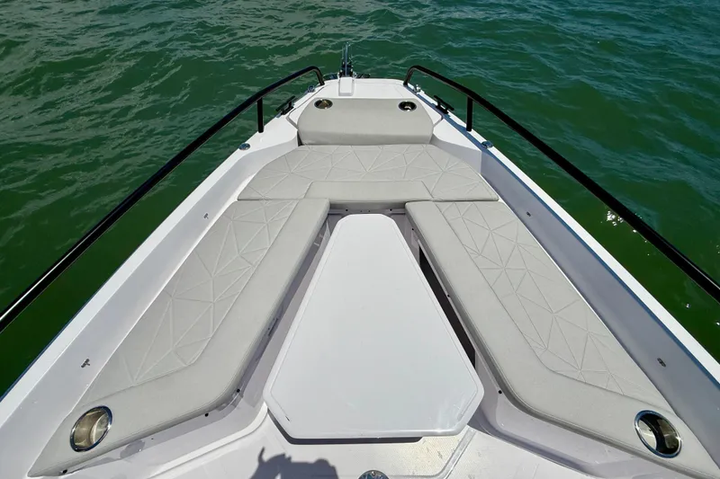 Slide: The Image of 2025 Axopar 29 Sun-Top boat bow with cushioned seating on calm water. - 16